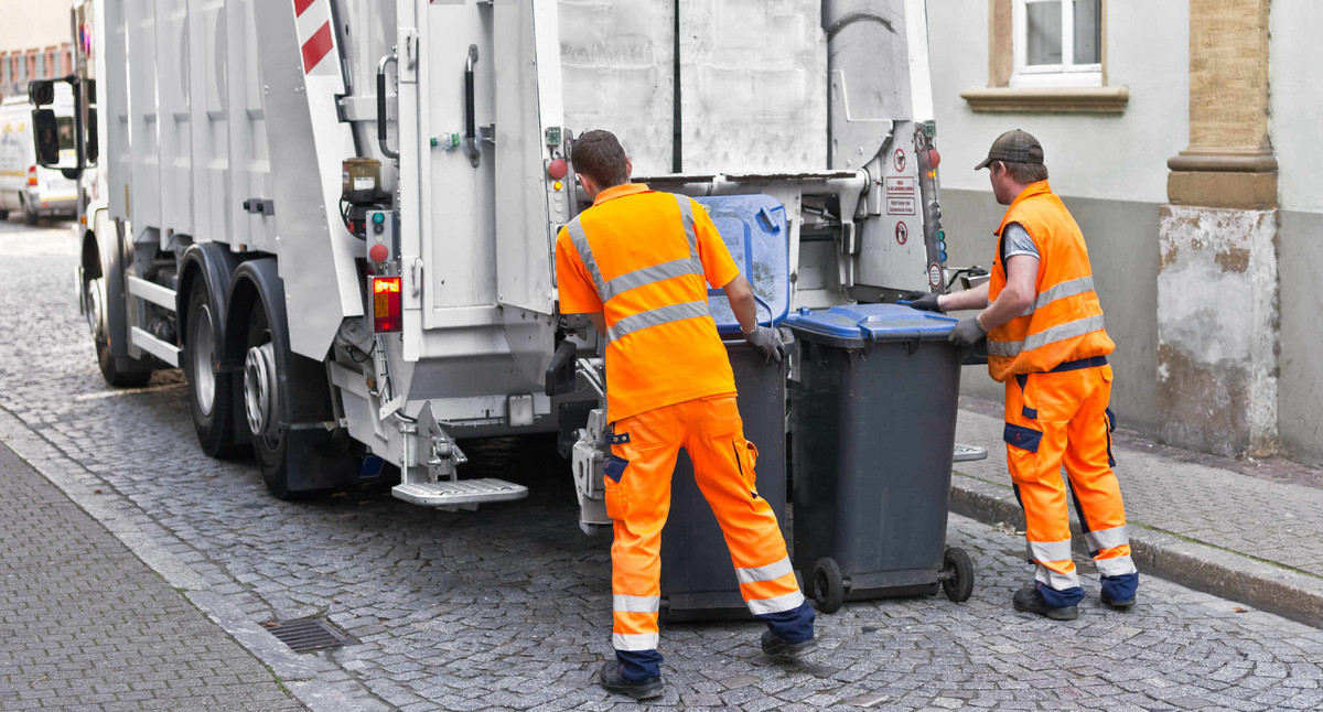 Zwei Männer stehen vor einem Müllfahrzeug und entleeren Mülltonnen