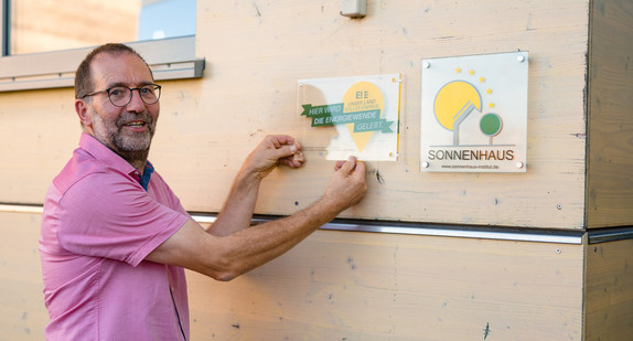 Geschäftsführer Thomas Hartmann mit seiner Plakette „Unser Land. Voller Energie“. Umweltstaatssekretär Andre Baumann hat die Hartmann Energietechnik GmbH als „Ort voller Energie“ ausgezeichnet. 