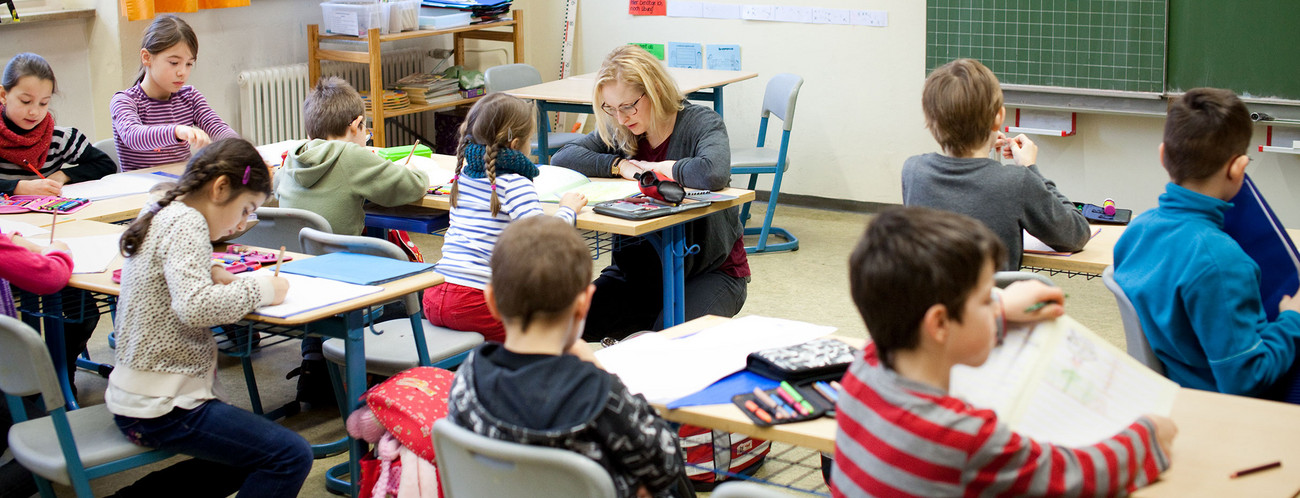 Eine Grundschullehrerin erklärt Schülerinnen und Schülern Aufgaben.