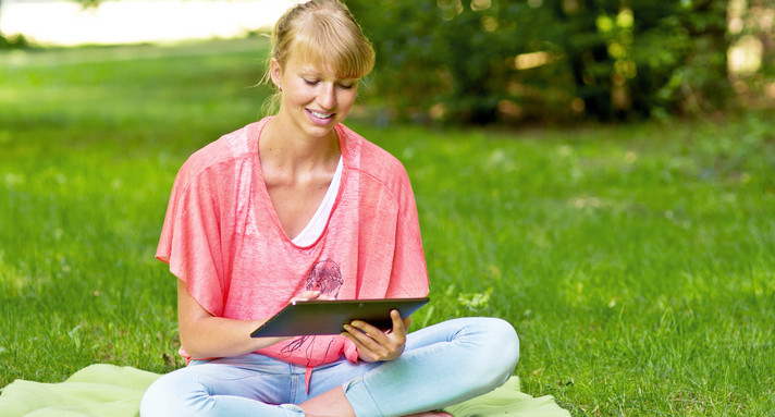 Frau sitzt mit Tablet auf Wiese