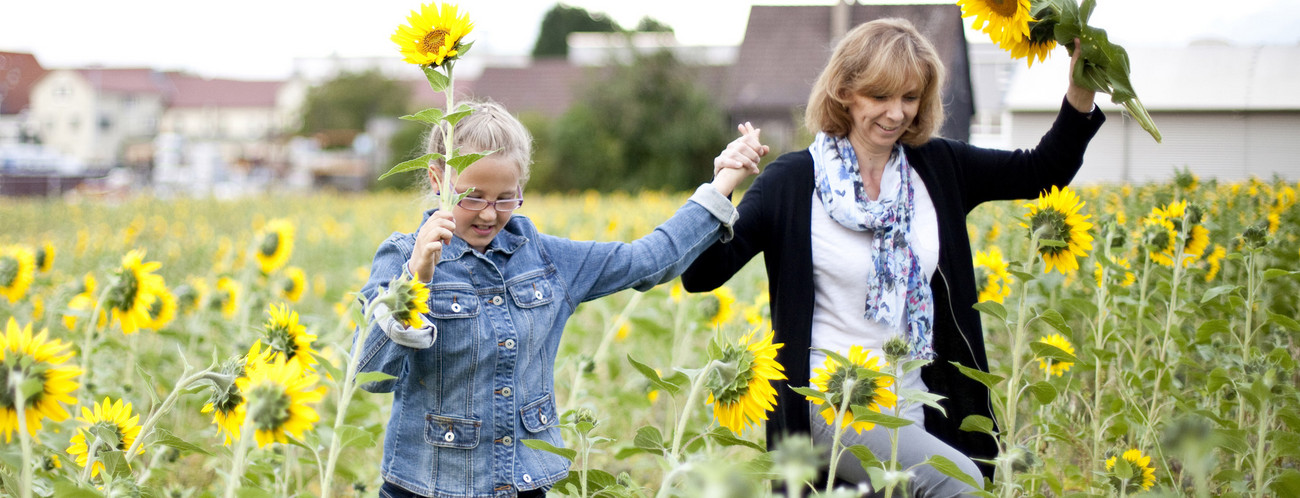 Eine Mutter die mit ihrem Kind über ein Sonnenblumenfeld läuft