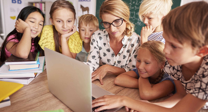 Lehrerin sitzt mit Schülern vor einem Laptop