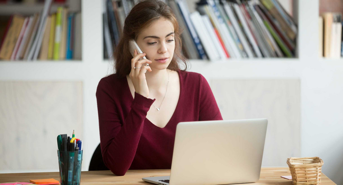 junge Frau arbeitet am Laptop und telefoniert mit Kunden