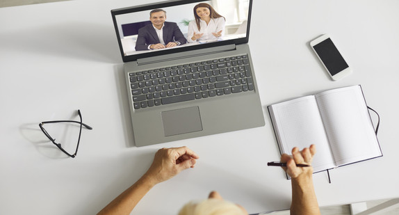 Person sitzt vor einem Laptop während einer Videokonferenz mit ihren Kollegen