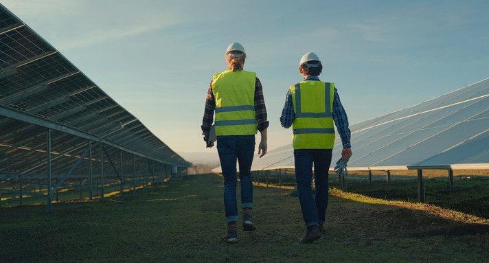 zwei Arbeitende begutachten eine Photovoltaik-Freiflächenanlage