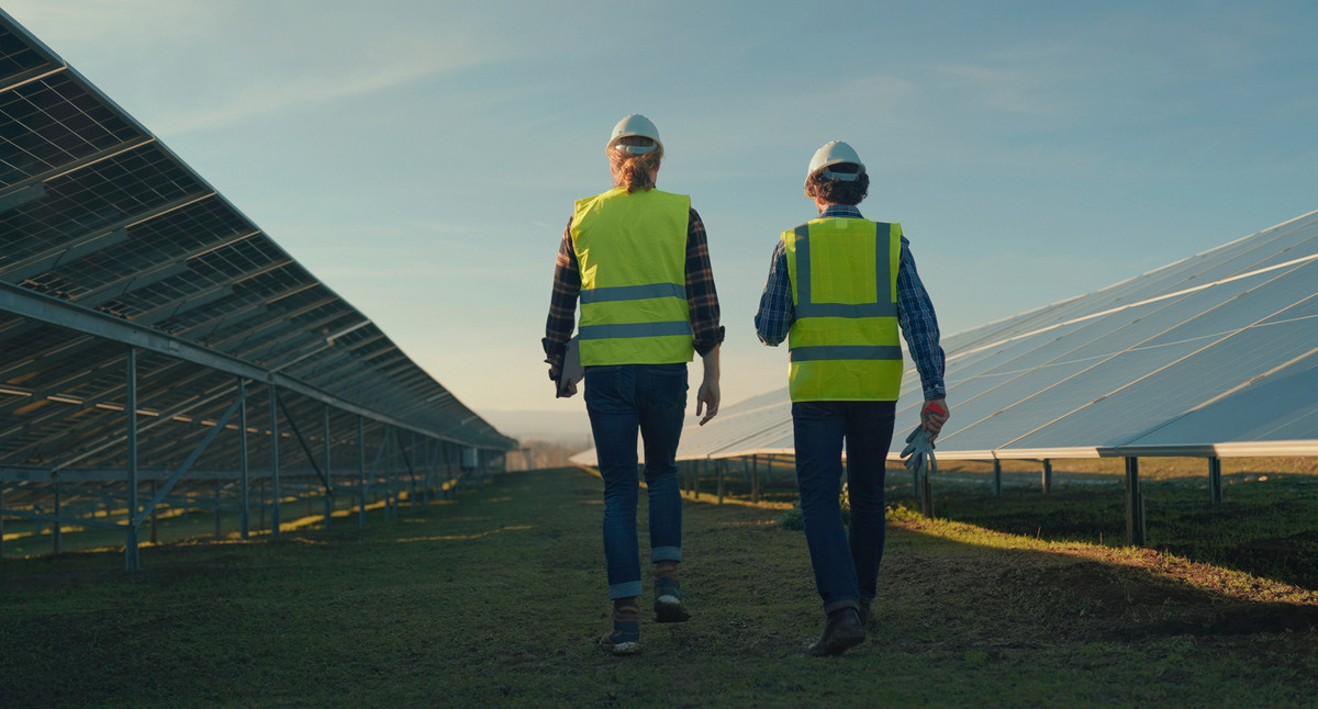 zwei Arbeitende begutachten eine Photovoltaik-Freiflächenanlage