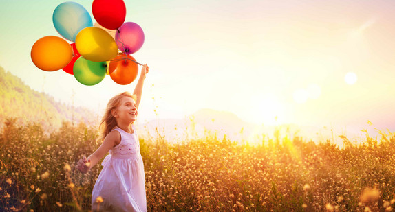 Mädchen mit Luftballons läuft im Sonnenuntergang über eine Wiese