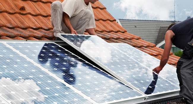 Handwerker verlegen Solarmodule auf einem Dach']