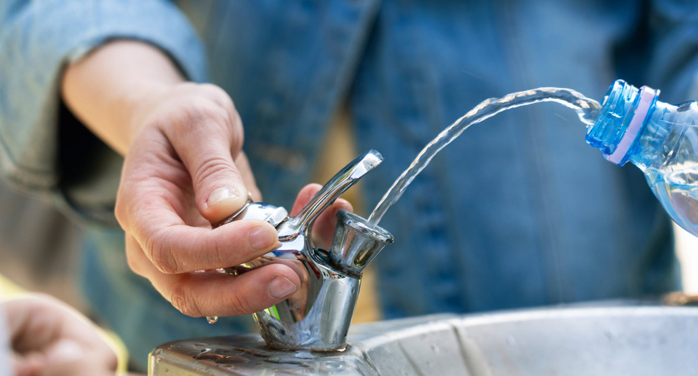 Eine Person füllt eine Flasche mit Trinkwasser aus einem öffentlichen Trinkbrunnen