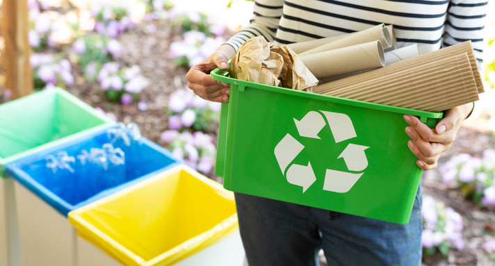 Frau hält grünen Korb mit einem Recyclingzeichen gefüllt mit Papier in Händen