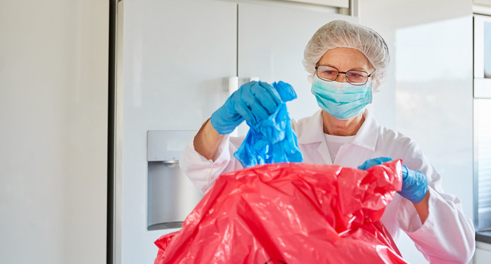 Reinigungskraft in Schutzkleidung entsorgt Einweghandschuhe in Klinik