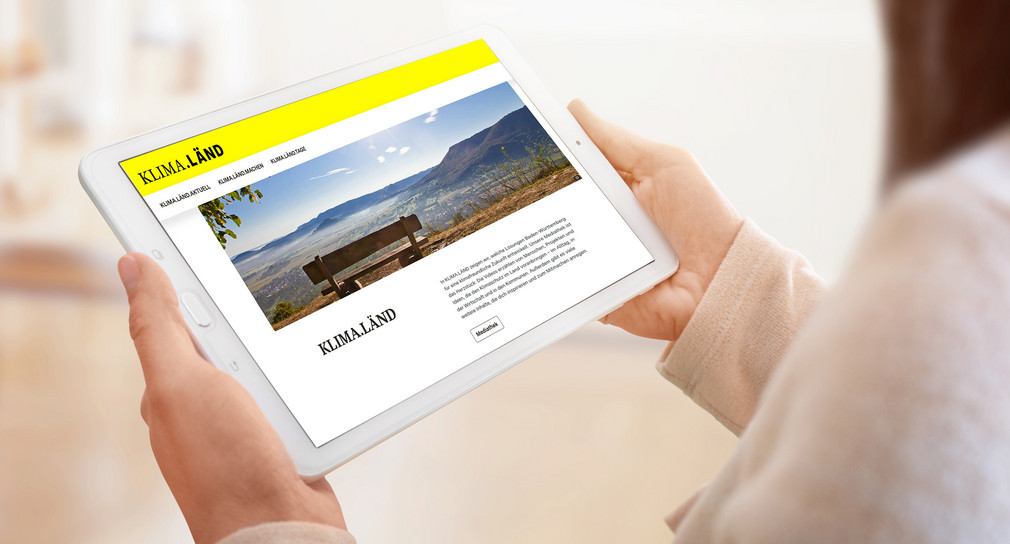 Eine Frau hält ein Tablet, auf dem die Internetseite KLIMA.LÄND geöffnet ist.