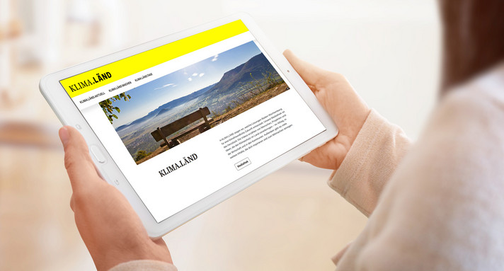 Eine Frau hält ein Tablet, auf dem die Internetseite KLIMA.LÄND geöffnet ist.