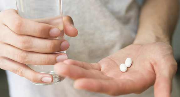 Hand mit Tabletten und Wasserglas