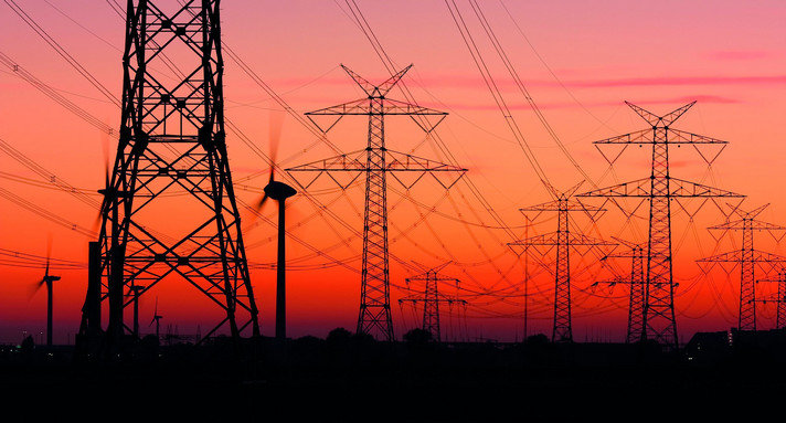 Strommasten bei Sonnenuntergang mit Windrädern